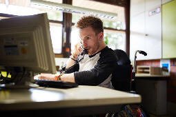 Junger Mann, der am Computer sitzt und telefoniert